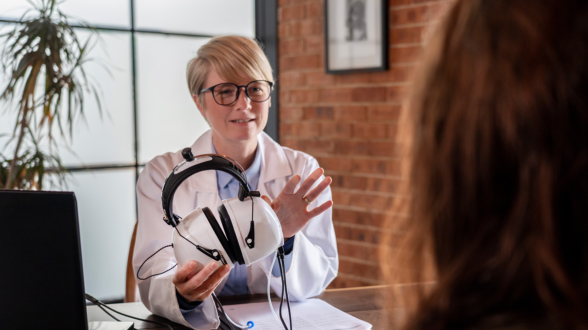 Clinical technologist in a lab coat presenting diagnostic equipment during a patient consultation